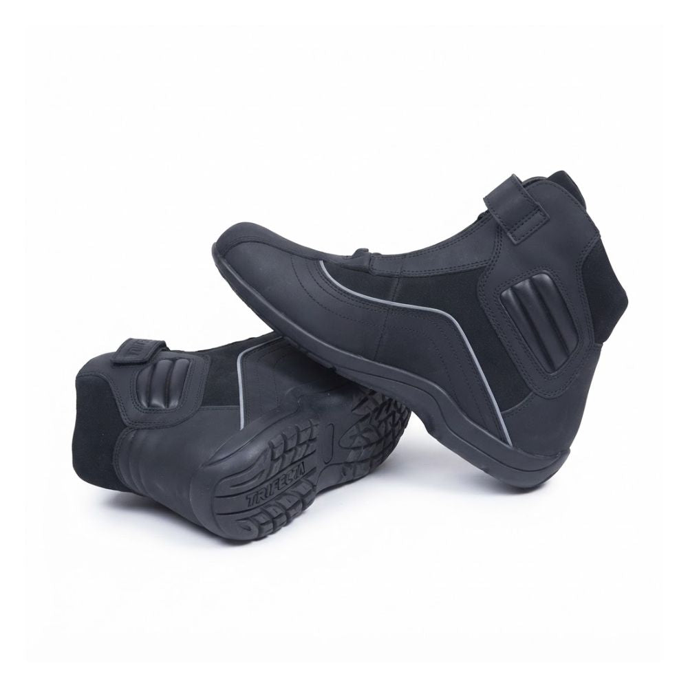 A pair of black ankle-high protective boots, one standing upright and the other lying on its side to show the treaded sole, set against a plain white background.