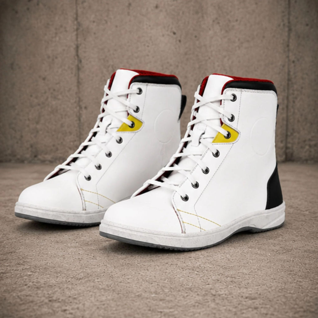 A pair of white high-top sneakers with black and red accents, featuring yellow logo details on the side, photographed on a textured concrete floor against a concrete wall.