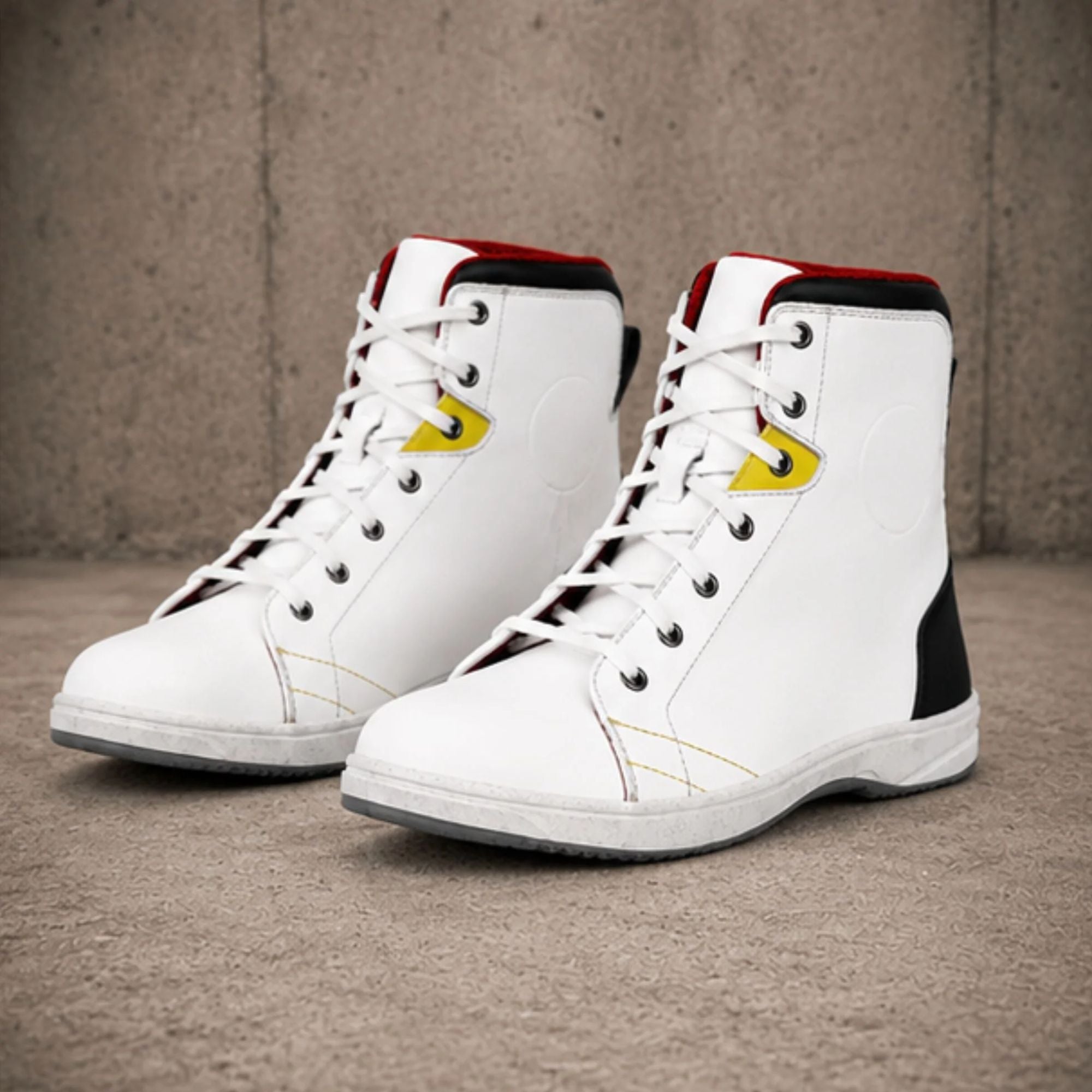 A pair of white high-top sneakers with black and red accents, featuring yellow logo details on the side, photographed on a textured concrete floor against a concrete wall.
